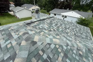 Close-up of a new asphalt shingle roof with varied shades of green, gray, and tan, showing overlapping patterns.